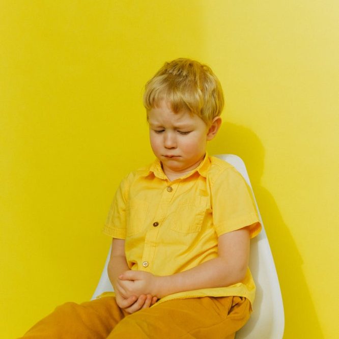 boy in yellow button up shirt sitting on white chair near wall